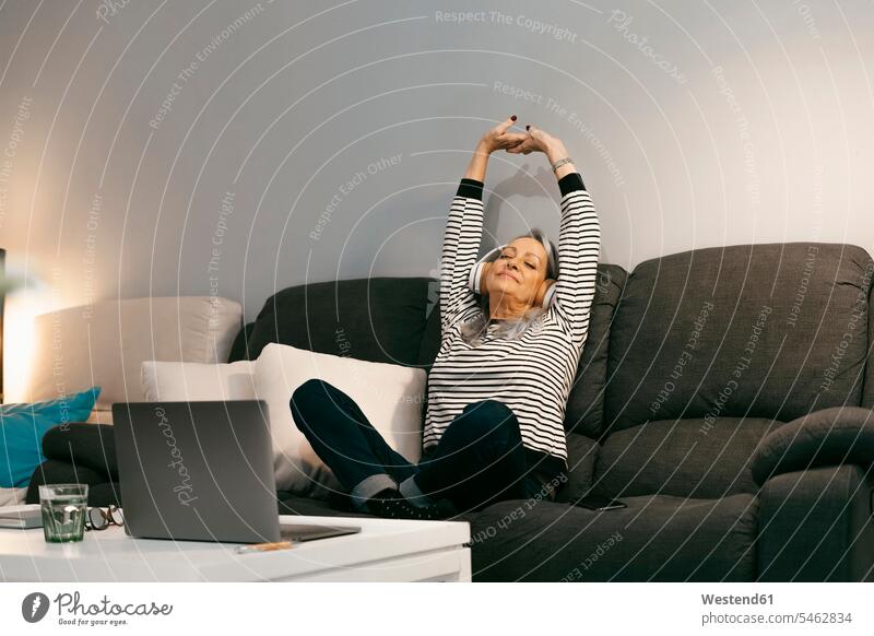 Carefree woman with hand raised listening music while sitting on sofa at home color image colour image indoors indoor shot indoor shots interior interior view