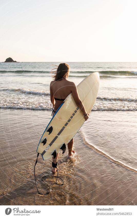 Young woman walking in water, carrying surfboard surfboards Sea ocean beach beaches going young women young woman surfing surf ride surf riding Surfboarding