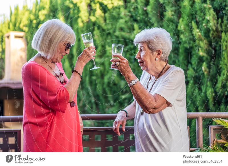 Senior female friends toasting champagne flutes while standing by railing in balcony color image colour image Spain leisure activity leisure activities