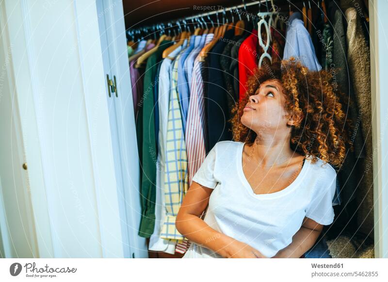 Young woman with curly hair at home looking at clothing in her wardrobe females women curls curled clothes Apparel eyeing Adults grown-ups grownups adult people