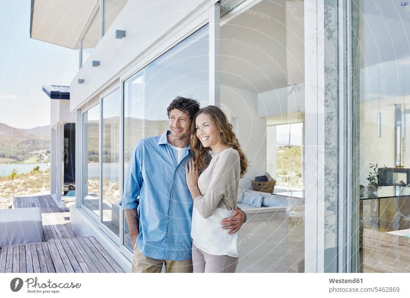 Happy couple standing at luxury beach house touristic tourists windows smile embrace Embracement hug hugging relax relaxing relaxation delight enjoyment