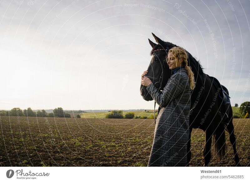 Affectionate young woman with horse on a field in the countryside smile in the evening Late Evening delight enjoyment Pleasant pleasure indulgence indulging
