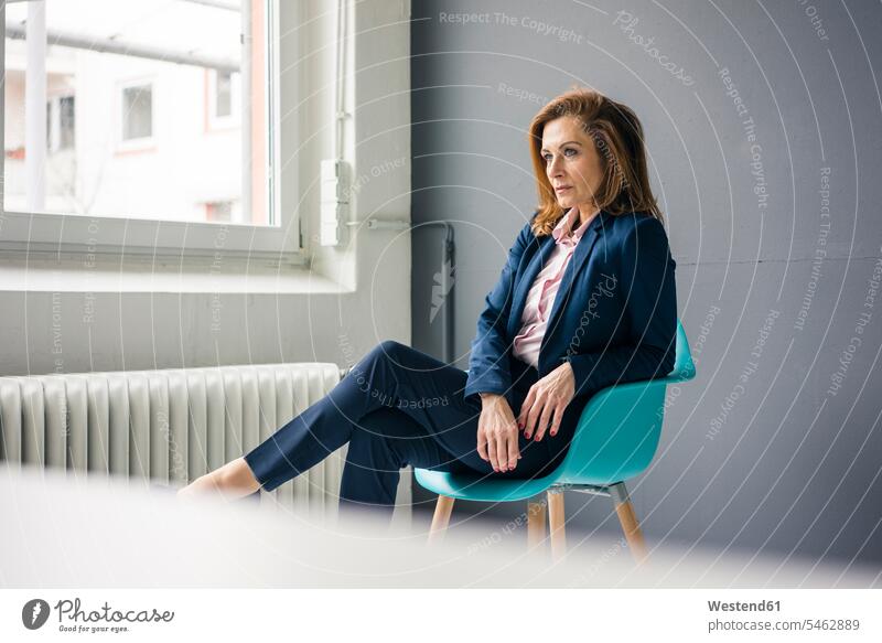 Displeased businesswoman sitting on a chair next to the window in her office serious earnest Seriousness austere displeased annoyed irritated annoying offices