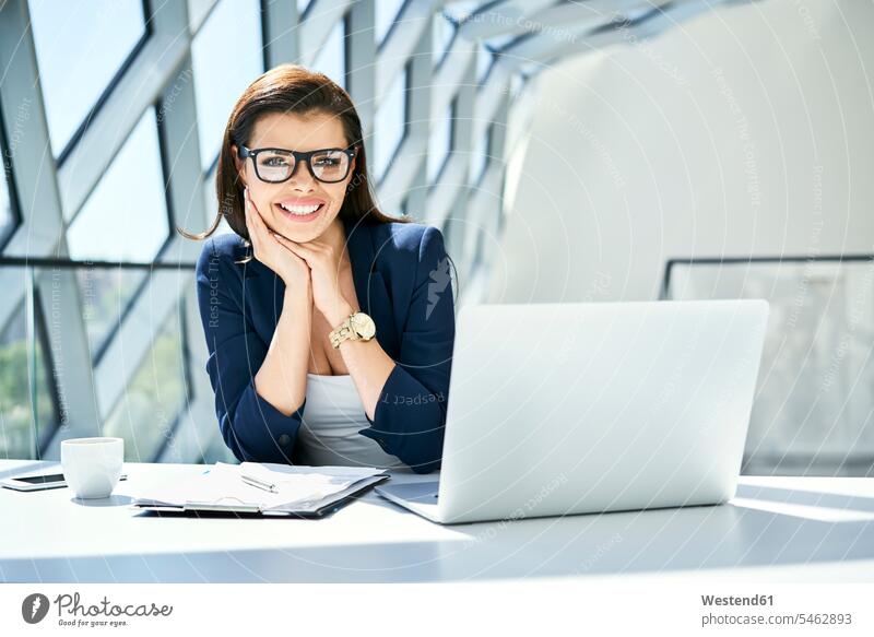 Portrait of smiling businesswoman sitting at desk in modern office smile offices office room office rooms desks contemporary businesswomen business woman