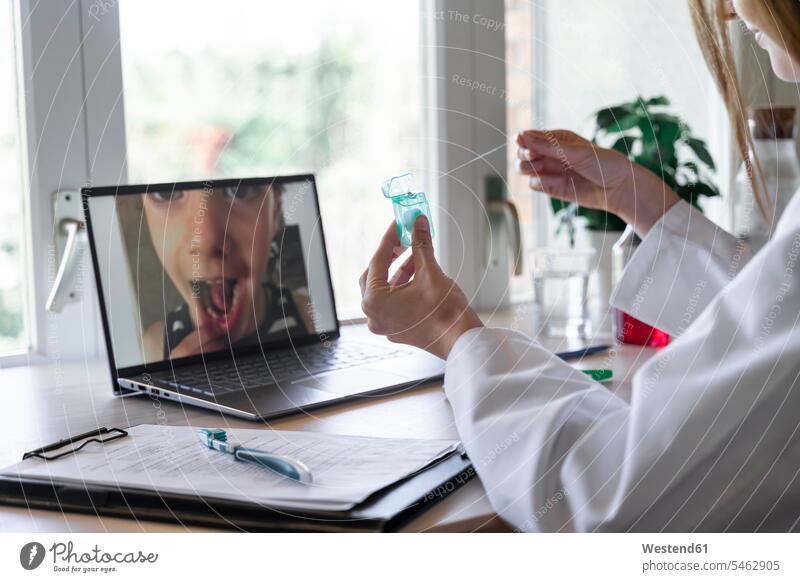 Young female dentist showing dental floss to patient through video call on laptop at home color image colour image indoors indoor shot indoor shots interior