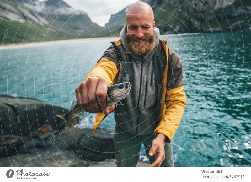 Norway, Lofoten, Moskenesoy, Young man holding freshly caught fish fishhook fish hook fish hooks Fishing Hooks fishhooks fishing hook Lofoten Islands Fishes