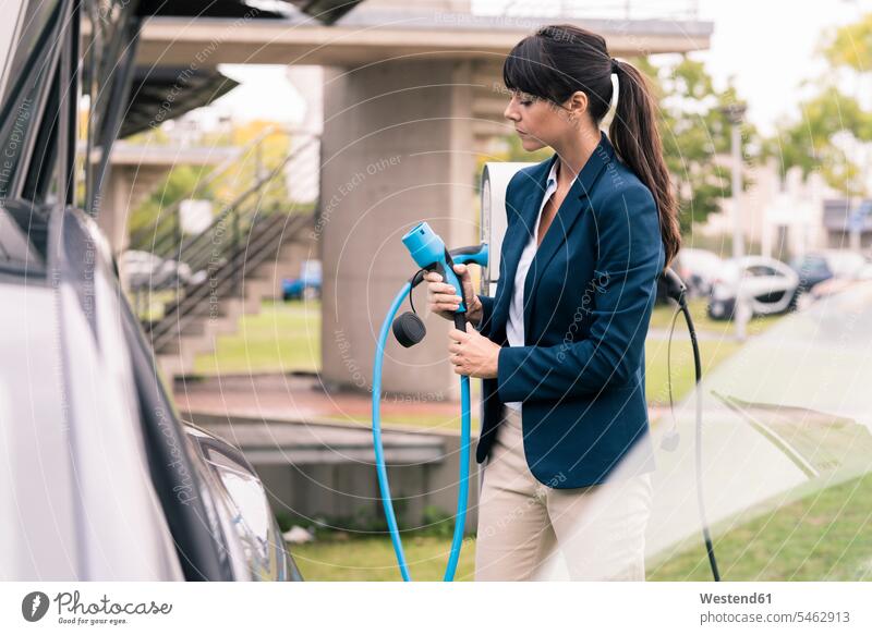 Businesswoman holding electric car charger at station color image colour image outdoors location shots outdoor shot outdoor shots day daylight shot