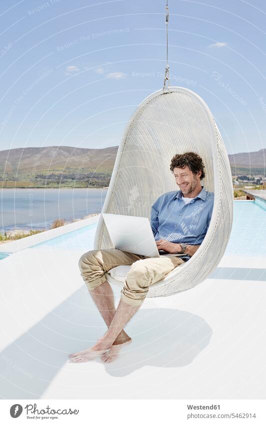 Man sitting in hanging chair above swimming pool using laptop touristic tourists business life business world business person businesspeople Business man