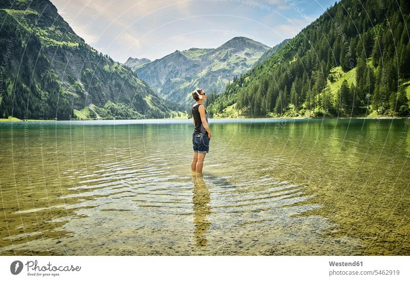 Mature woman standing knee deep in Vilsalpsee while listening music on sunny day color image colour image Austria outdoors location shots outdoor shot