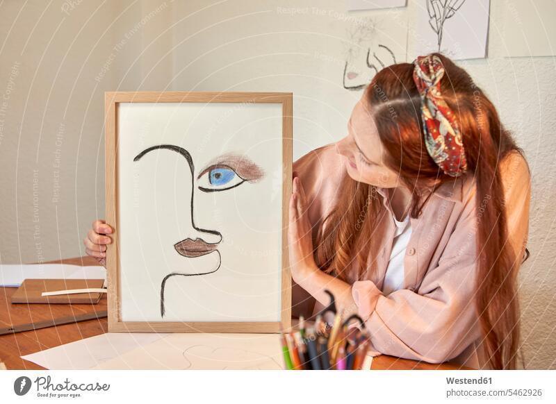 Female artist showing drawing art picture frame against wall at home color image colour image indoors indoor shot indoor shots interior interior view Interiors