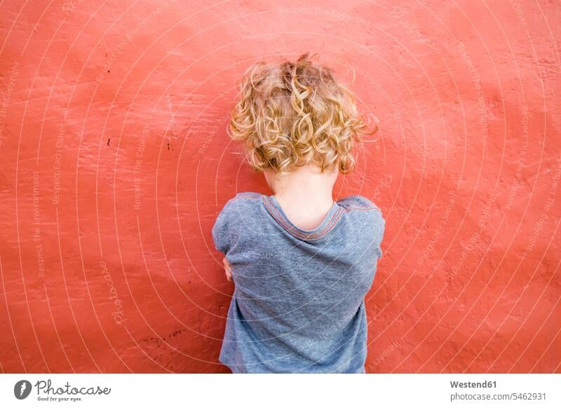 Back view of little boy standing in front of red wall T- Shirt t-shirts tee-shirt solitary reclusive reclusively Emotions Feeling Feelings Sentiment Sentiments