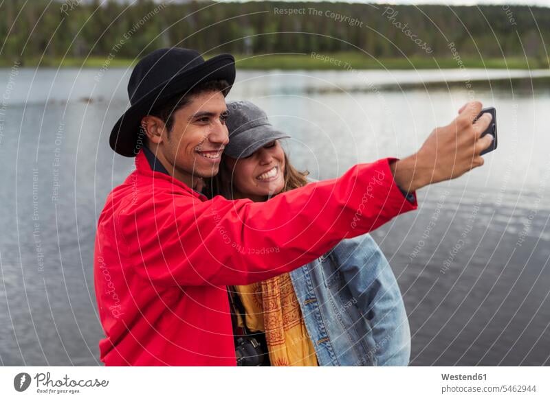 Finland, Lapland, happy couple taking a selfie at a lake lakes twosomes partnership couples happiness Selfie Selfies water waters body of water people persons