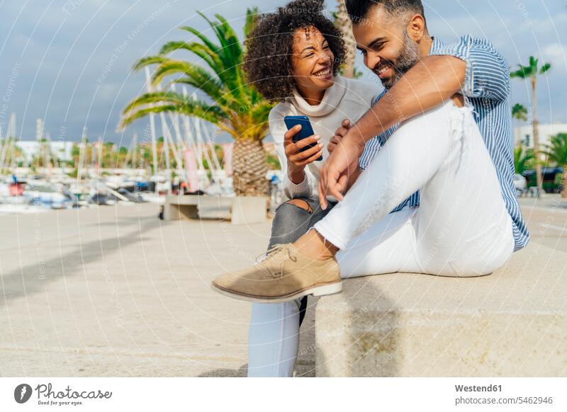 Spain, Barcelona, happy couple with cell phone at the marina happiness mobile phone mobiles mobile phones Cellphone cell phones twosomes partnership couples