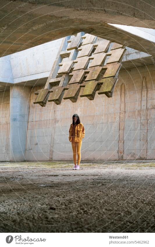 Young woman wearing yellow jeans clothes, standing in concrete building females women Denim Jeans Adults grown-ups grownups adult people persons human being