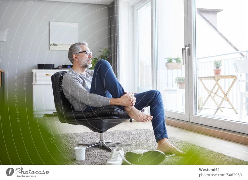 Mature man relaxing on leather chair in his living room looking out of window living rooms livingroom men males leather chairs relaxation relaxed view seeing
