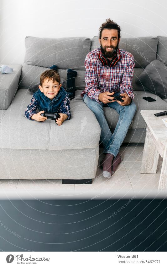 Portrait of father and son playing computer game together on the couch pa fathers daddy papa computer games settee sofa sofas couches settees sons manchild