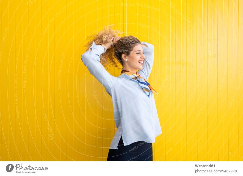 Smiling young woman tying her hair in front of yellow background human human being human beings humans person persons caucasian appearance caucasian ethnicity