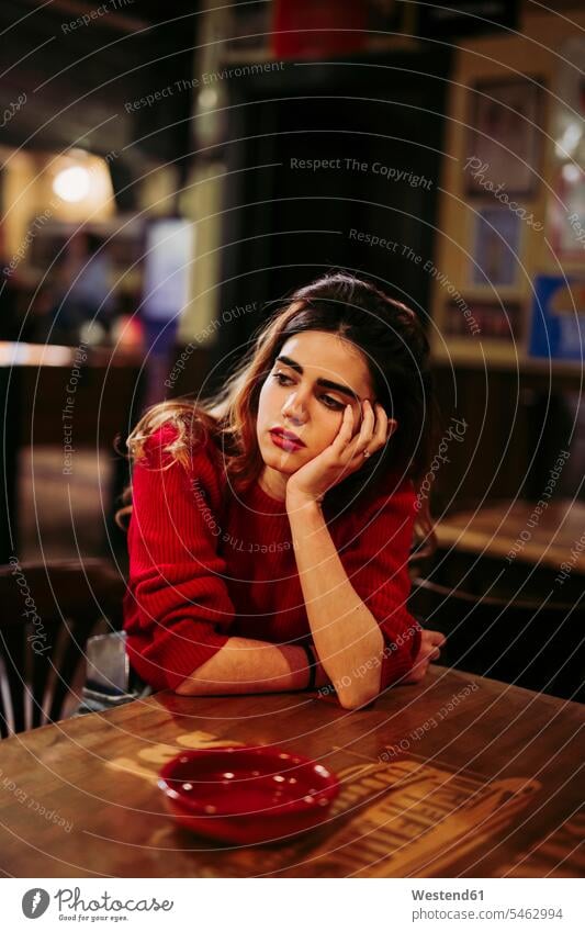 Sad thoughtful mid adult woman with hand on chin sitting at table in restaurant color image colour image Spain leisure activity leisure activities free time