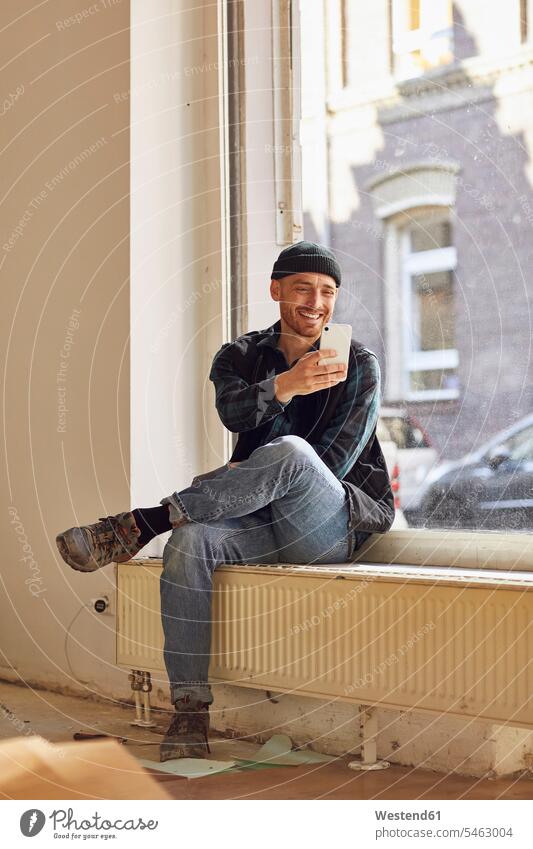 Man refurbishing shop location, sitting on windowsill, using smartphone human human being human beings humans person persons caucasian appearance