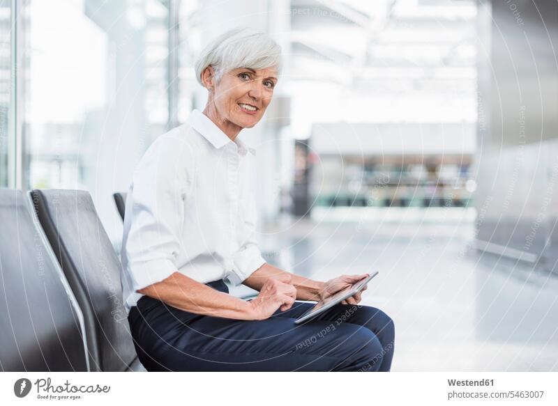Smiling senior businesswoman sitting in waiting area using tablet businesswomen business woman business women digitizer Tablet Computer Tablet PC
