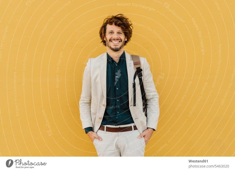 Portrait of laughing businessman with backpack standing in front of yellow wall business life business world business person businesspeople Business man