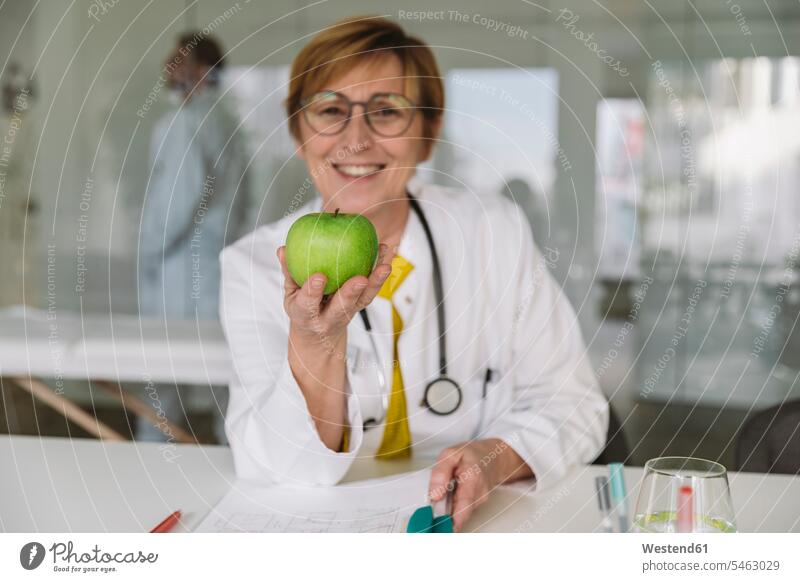 Doctor sitting at desk holding an apple Occupation Work job jobs profession professional occupation glass panes health healthcare Healthcare And Medicines
