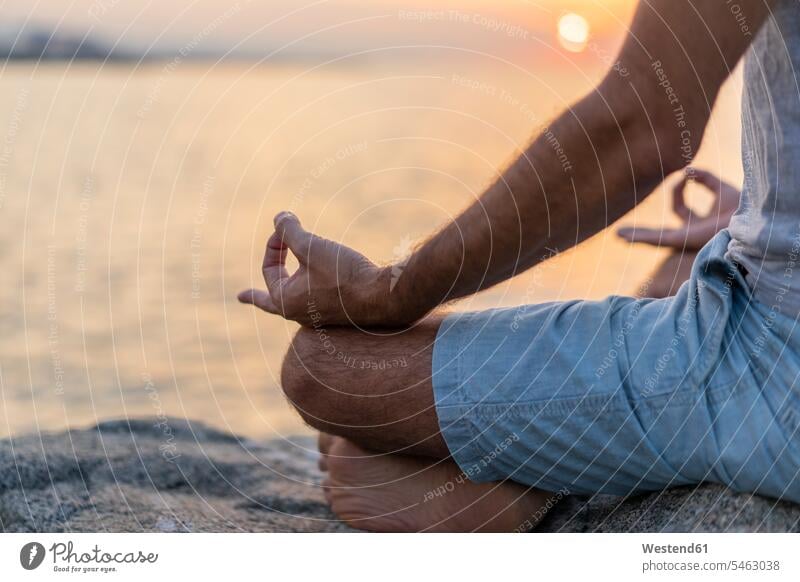 Spain. Man meditating during sunrise on rocky beach, mudra sitting Seated man men males meditation meditations meditate Hand Posture yoga Mudra Adults grown-ups