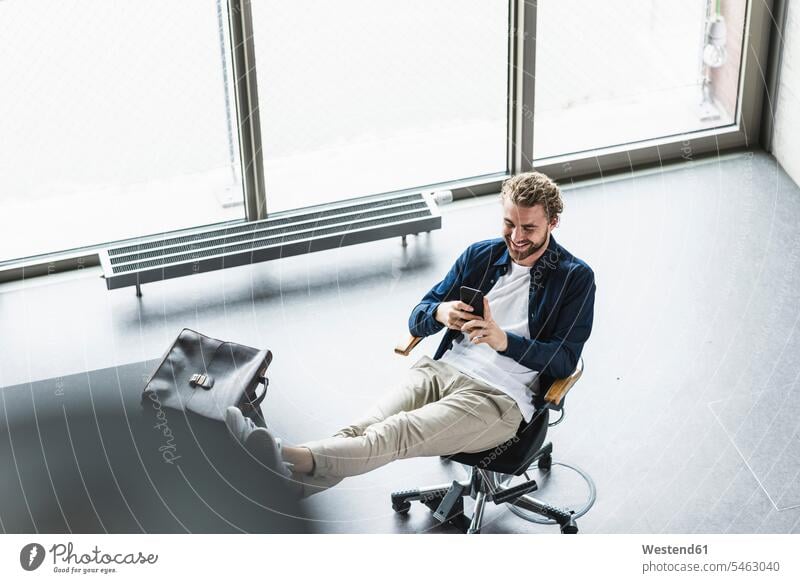 Smiling casual businessman sitting in office with feet up using cell phone Businessman Business man Businessmen Business men offices office room office rooms