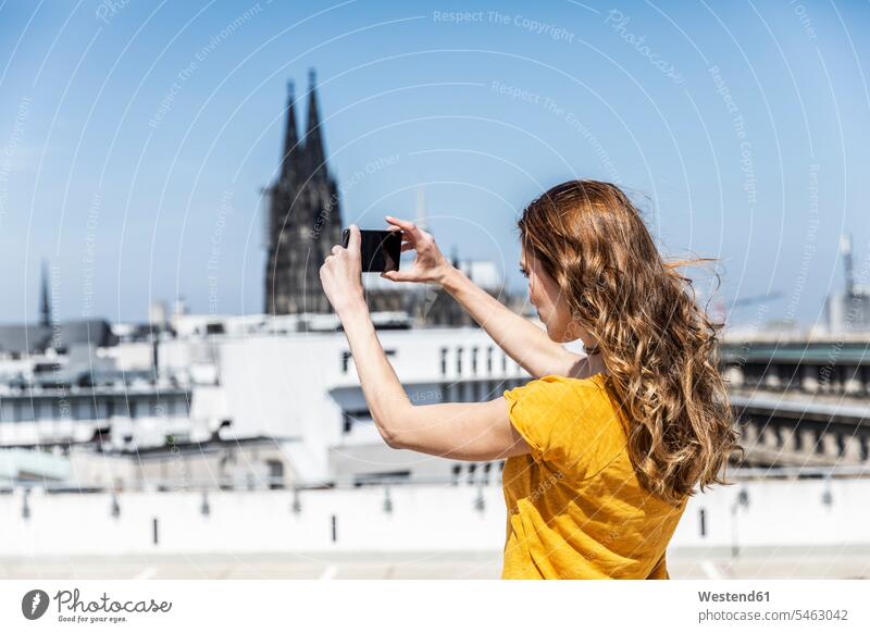 Germany, Cologne, woman taking photo with smartphone on roof terrace females women Smartphone iPhone Smartphones photographing deck rooftop Adults grown-ups