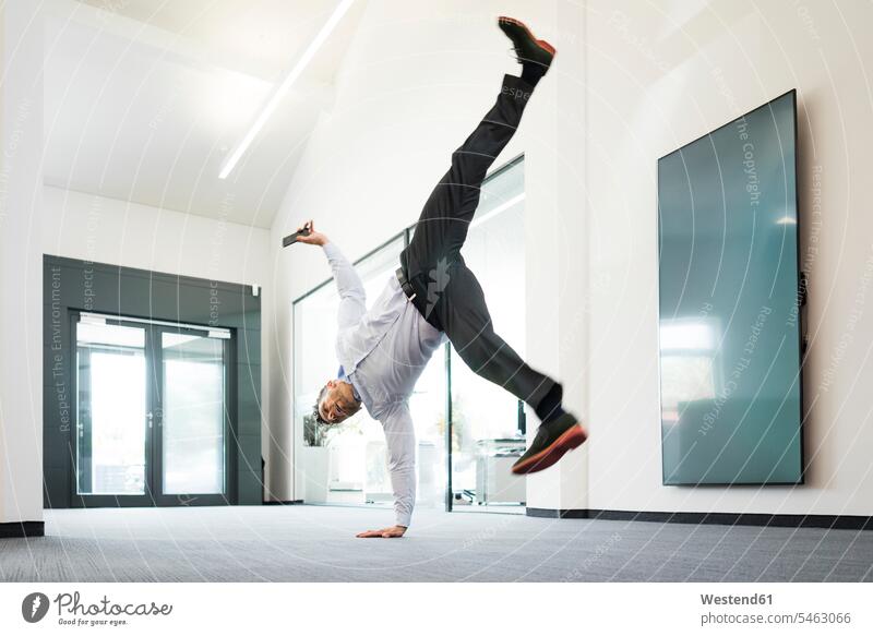 Businessman with cell phone doing a one-handed handstand on office floor Occupation Work job jobs profession professional occupation business life