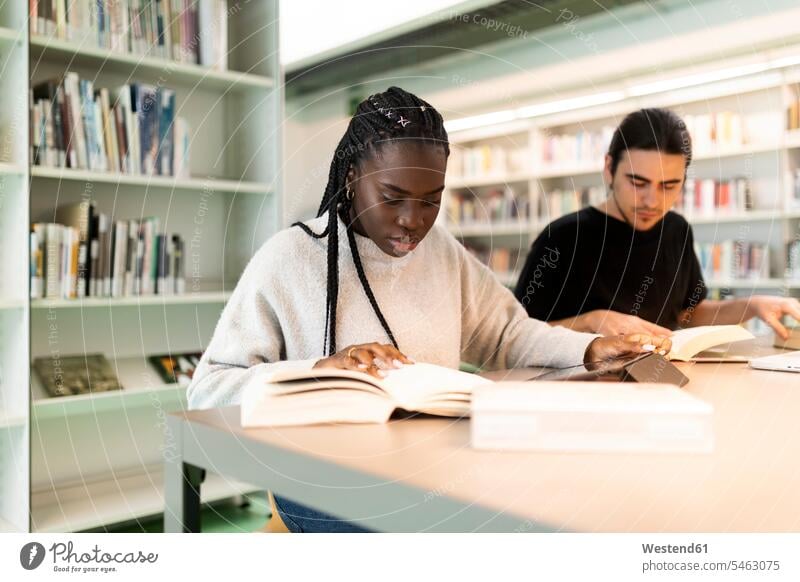 Two students learning in a library friends mate books Tables read Seated sit study concentrate concentrated concentrating Lifestyle indoor indoor shot