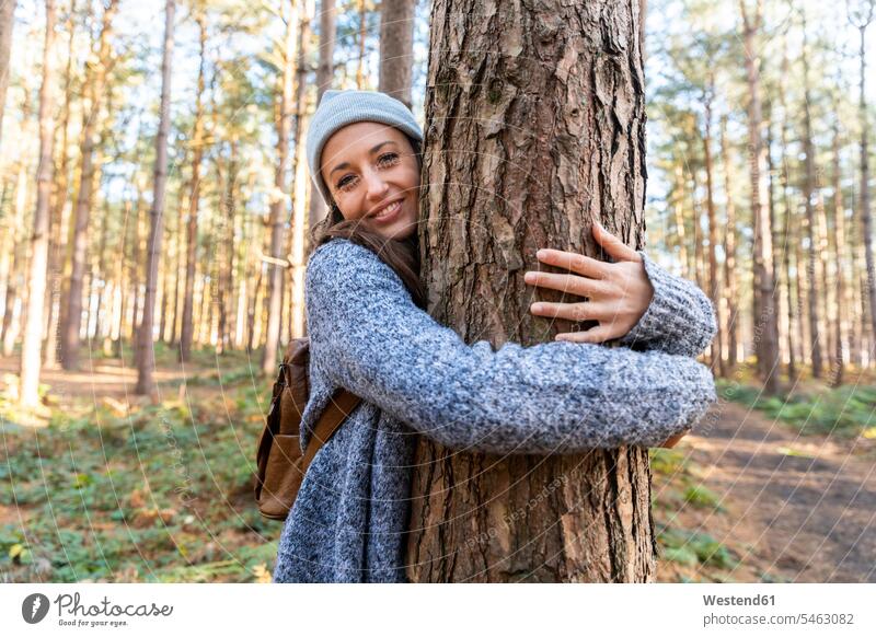 Smiling female hiker embracing tree trunk while exploring in Cannock Chase woodland color image colour image outdoors location shots outdoor shot outdoor shots