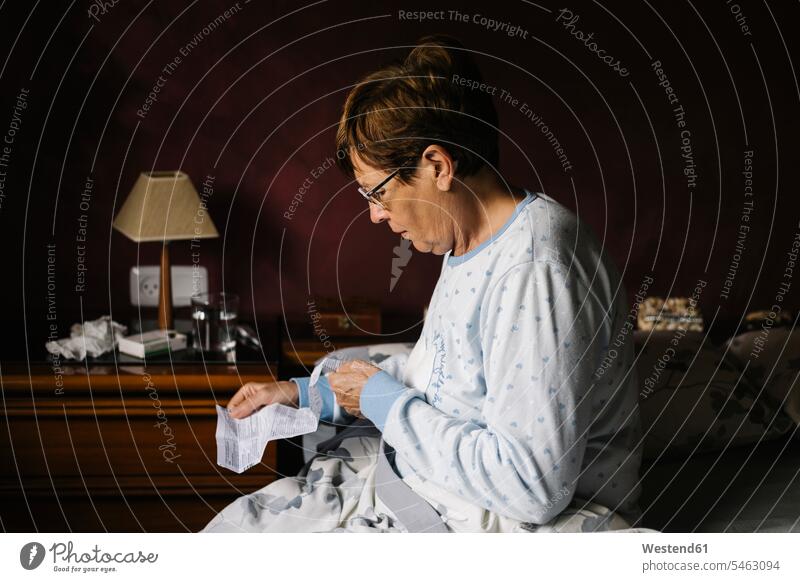 Ill senior woman reading instructions of prescription medicine while sitting on bed at home color image colour image Spain healthcare and medicine medical