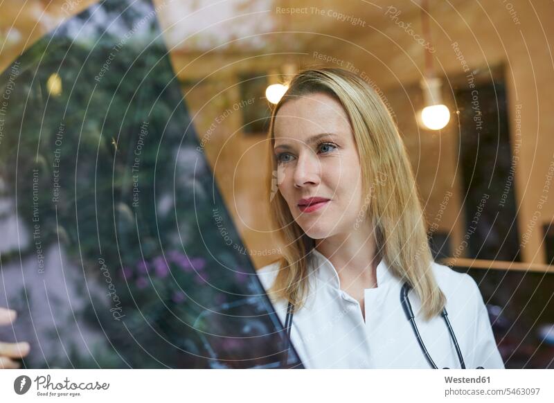 Female doctor looking at x-ray image behind windowpane x-rays radiography radiographies woman females women eyeing window glass window glasses windowpanes