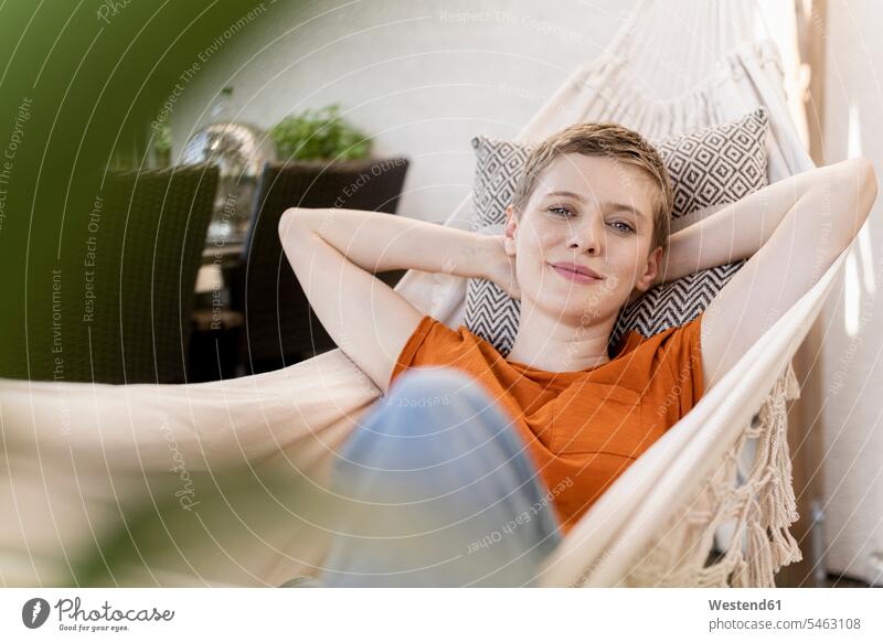 Smiling beautiful woman with hands behind head resting on hammock in porch color image colour image Germany leisure activity leisure activities free time