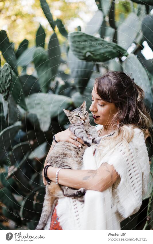 Woman holding cat while standing against plant color image colour image casual clothing casual wear leisure wear casual clothes Casual Attire beautiful Woman
