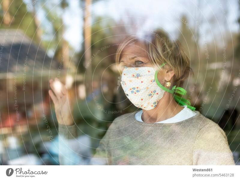 Mature woman with face mask looking through window glass during COVID-19 pandemic color image colour image domestic life at home domestic scene quarantine