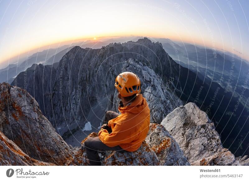 Climber with orange helmet sitting on Ellmauer Halt at sunrise, Wilder Kaiser, Ellmauer Halt, Tyrol, Austria Seated in the morning lyrical Romance sports