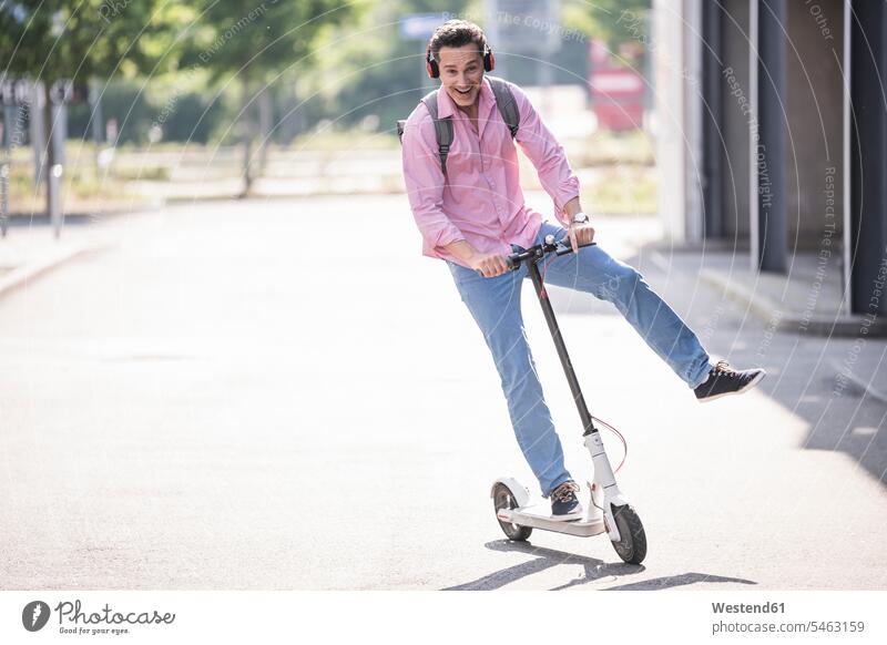 Businessman with headphones and backpack riding his E-Scooter human human being human beings humans person persons caucasian appearance caucasian ethnicity
