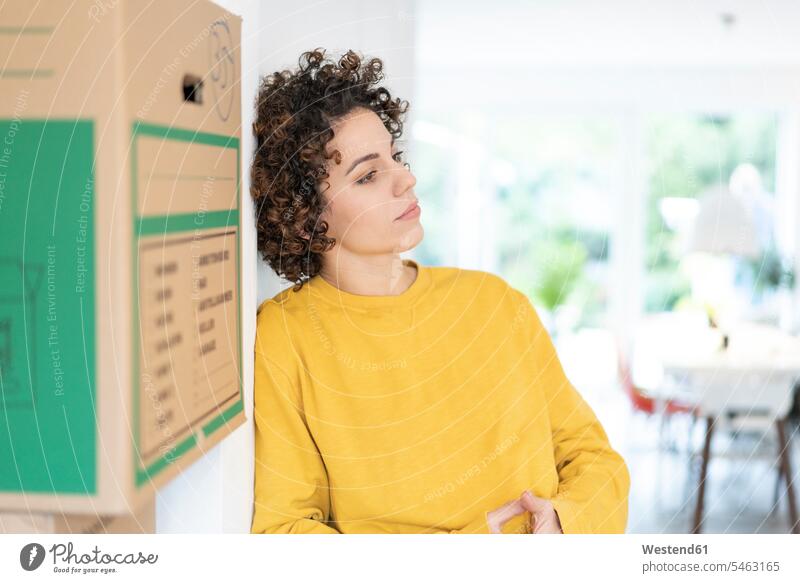 Serious woman leaning against a wall at home with cardboard boxes packing case packing cases females women serious earnest Seriousness austere walls Adults