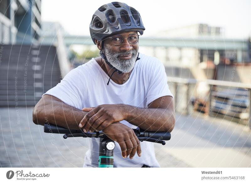 Portrait of smiling mature man wearing cycling helmet leaning on handlebar of Electric Scooter human human being human beings humans person persons Mixed Race