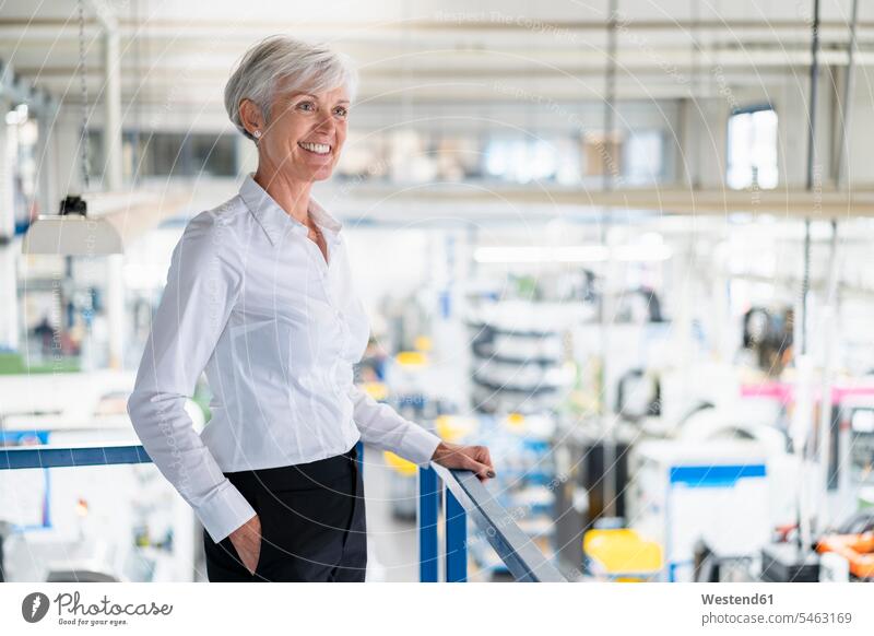 Smiling senior businesswoman on upper floor in factory overlooking shop floor factories businesswomen business woman business women smiling smile