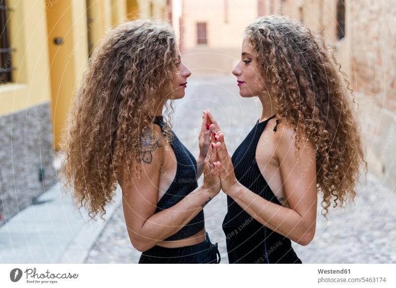Side view of twin sisters standing face to face touching hands human hand human hands people persons human being humans human beings twins siblings