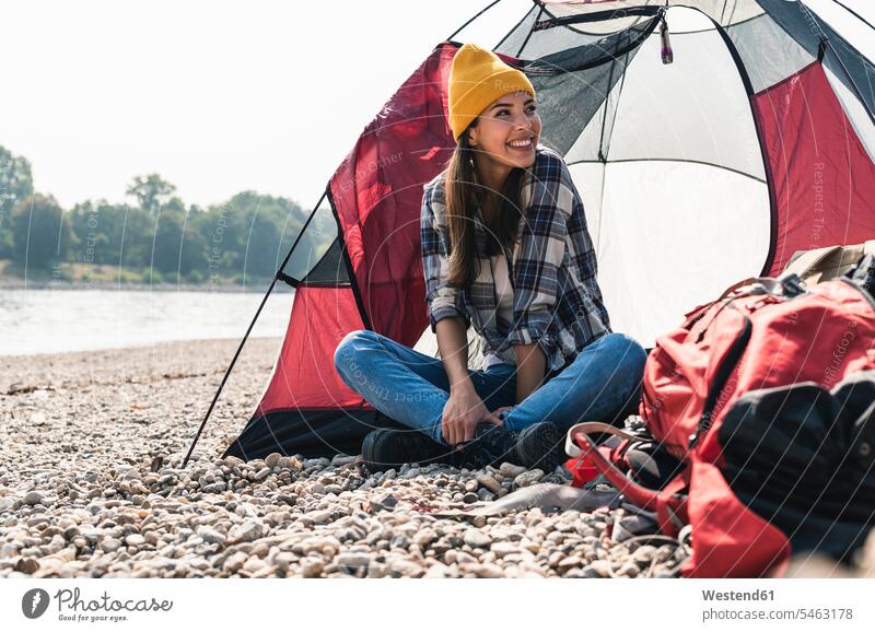 Happy young woman sitting at a tent at the riverside happiness happy tents riverbank Seated smiling smile females women water's edge waterside shore Adults
