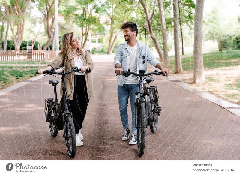 Smiling young couple with electric bicycles walking on road color image colour image Spain E-Bike Electric bicycle Electric Bike bike bikes Cycle transportation