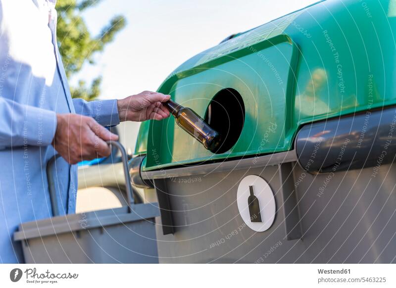 Close-up of man putting bottle into bottle bank material materials recources Bottles Glass Bottles shirts hold collect collected trash waste location shot