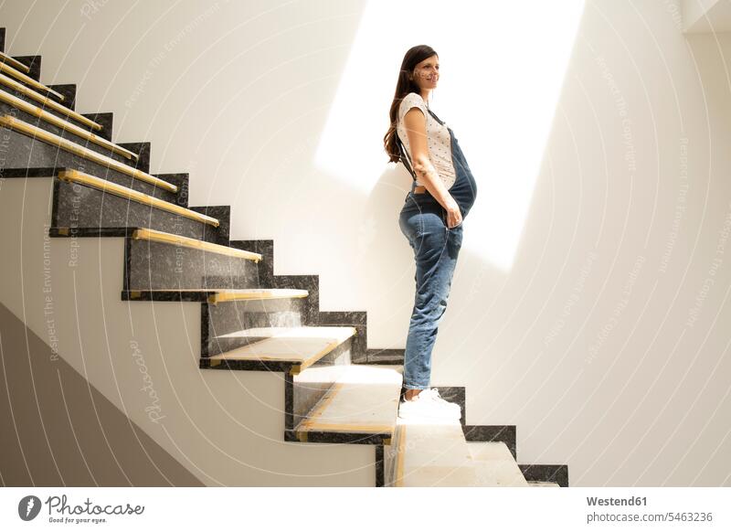 Thoughtful pregnant woman looking away while standing on staircase in new house color image colour image Germany indoors indoor shot indoor shots interior