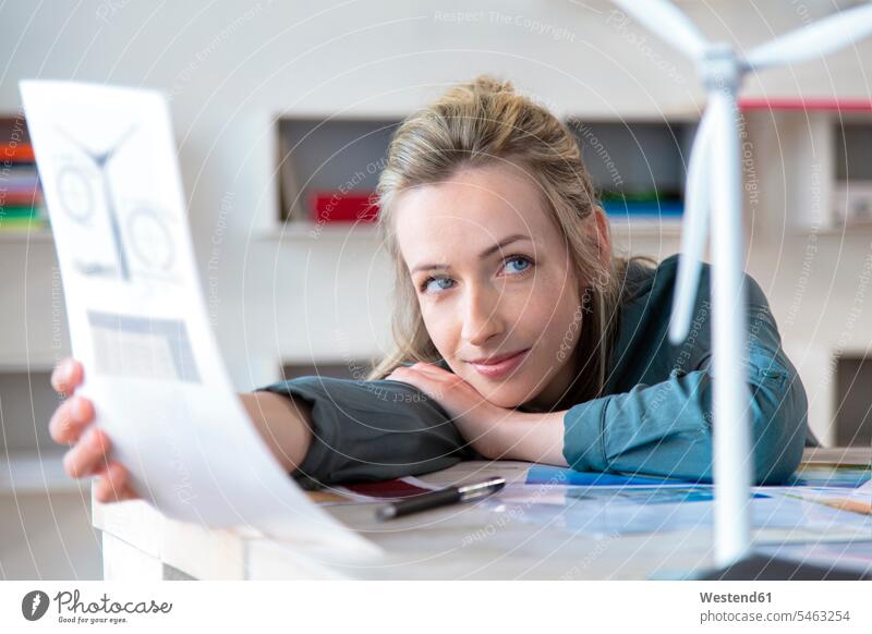 Portrait of woman leaning on desk in office with paper and wind turbine model human human being human beings humans person persons caucasian appearance