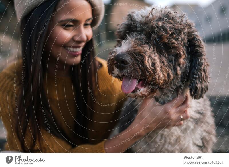 Happy young woman stroking her dog in the city friends animals creature creatures domestic animal pet Canine dogs caps hat hats smile delight enjoyment Pleasant