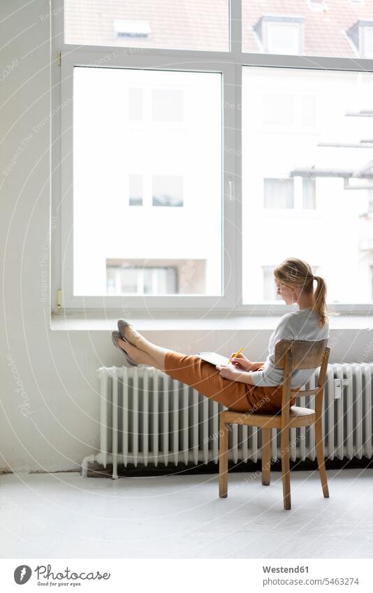 Young woman sitting on chair at the window in office taking notes business life business world business person businesspeople business woman business women